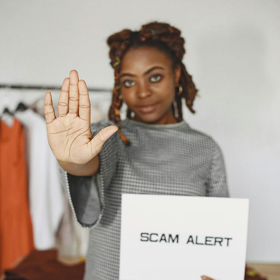 woman holding a scam alert sign with her other had up in a stop gesture.